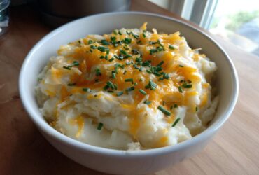 A white bowl filled with creamy easy crockpot potato soup topped with melted cheddar cheese and fresh chopped chives.