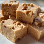 A stack of creamy, light brown maple fudge squares topped with chopped walnuts, ready to eat.