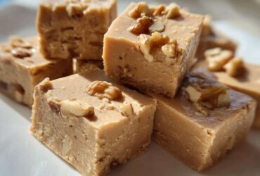 A stack of creamy, light brown maple fudge squares topped with chopped walnuts, ready to eat.