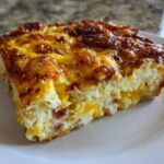A close-up of a hearty slice of breakfast egg bake with a deeply browned, cheesy top.