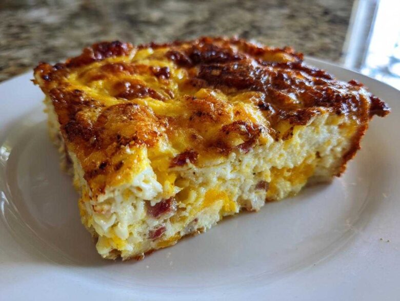 A close-up of a hearty slice of breakfast egg bake with a deeply browned, cheesy top.