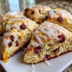 Close-up of several flaky cranberry orange scones drizzled with white glaze and garnished with orange zest.