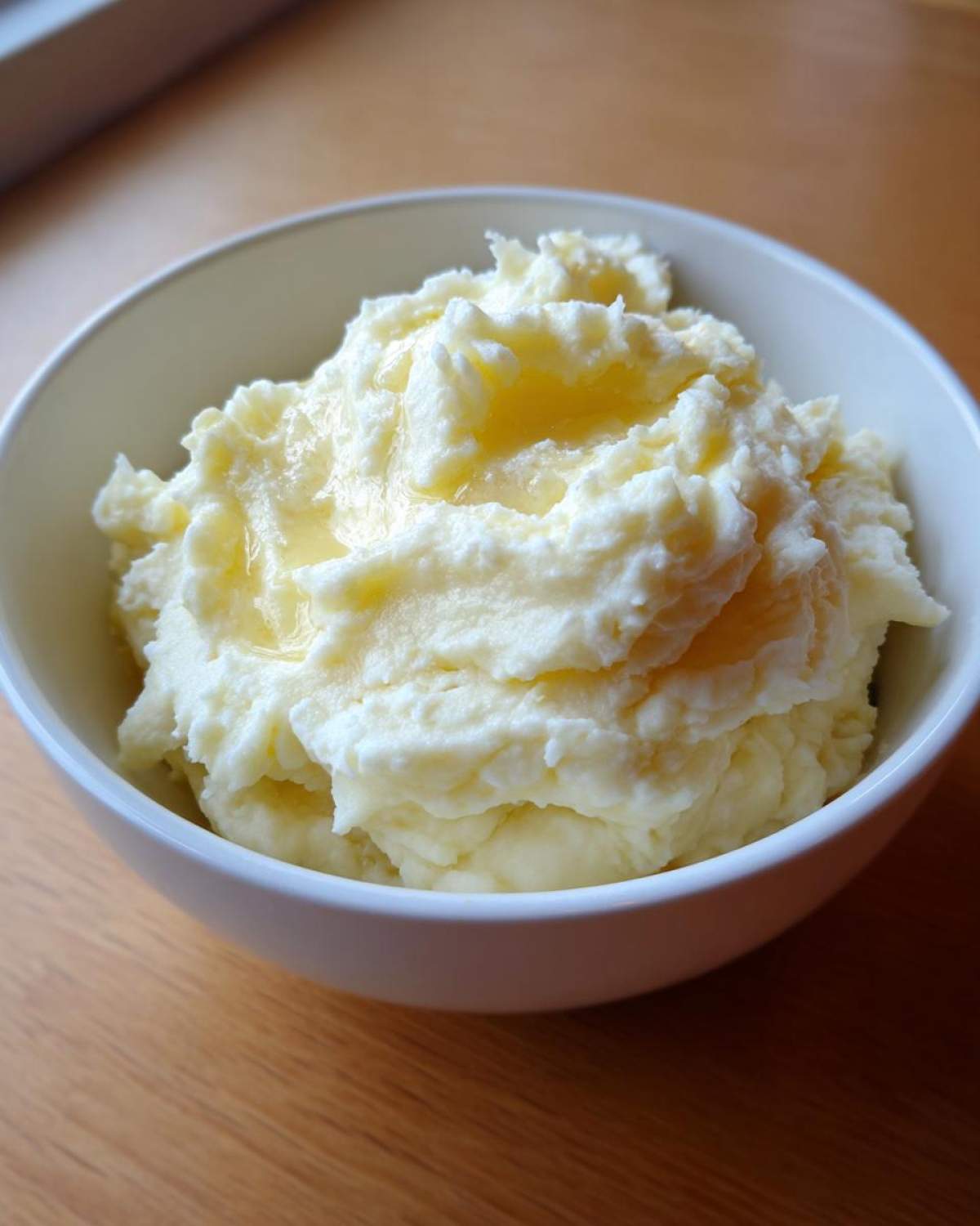 Close-up of creamy, fluffy mashed potatoes topped with melted butter served in a white bowl.