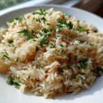 Close-up of fluffy, perfectly cooked rice pilaf garnished generously with chopped fresh parsley on a white plate.