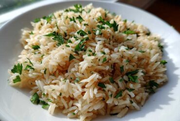 Close-up of fluffy, perfectly cooked rice pilaf garnished generously with chopped fresh parsley on a white plate.