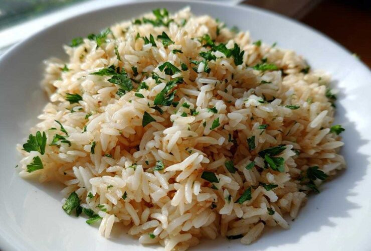 Close-up of fluffy, perfectly cooked rice pilaf garnished generously with chopped fresh parsley on a white plate.