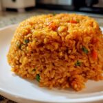 A perfectly molded mound of fluffy, orange-red Spanish rice served on a white plate.