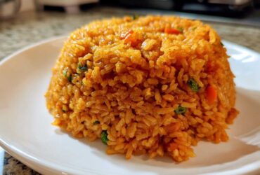 A perfectly molded mound of fluffy, orange-red Spanish rice served on a white plate.