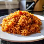 A close-up of a mound of perfectly cooked, fluffy spanish rice steaming on a white plate.