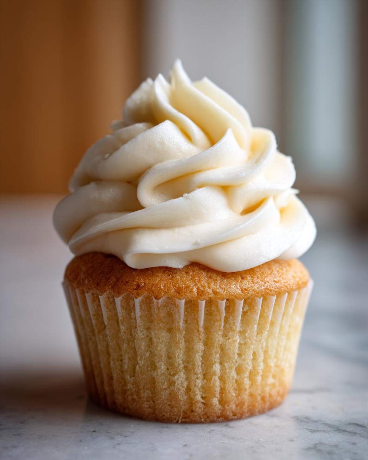 Close-up of a single, perfectly baked vanilla cupcake topped with a tall swirl of creamy white frosting.