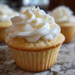 Close-up of a moist vanilla cupcake topped with a tall swirl of white vanilla buttercream frosting.