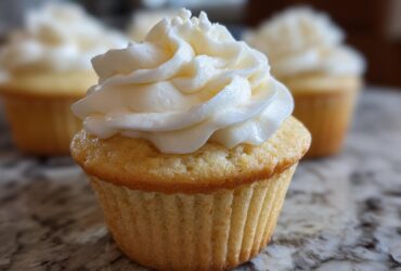 Close-up of a moist vanilla cupcake topped with a tall swirl of white vanilla buttercream frosting.