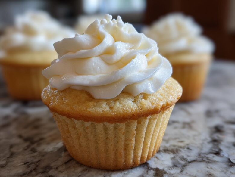 Close-up of a moist vanilla cupcake topped with a tall swirl of white vanilla buttercream frosting.