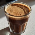 Close-up of a chilled Coffee Smoothie with rich brown foam topping in a faceted glass.