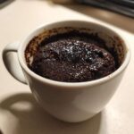 Close-up of a rich, dark chocolate mug cake fresh out of the microwave in a white mug, ready to eat.