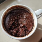 Overhead view of a fudgy chocolate mug cake, slightly broken open, topped with chocolate chips in a white mug.