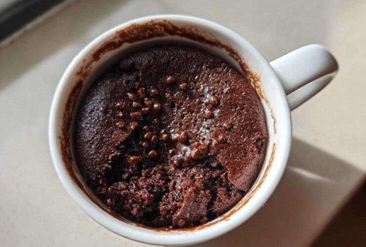 Overhead view of a fudgy chocolate mug cake, slightly broken open, topped with chocolate chips in a white mug.