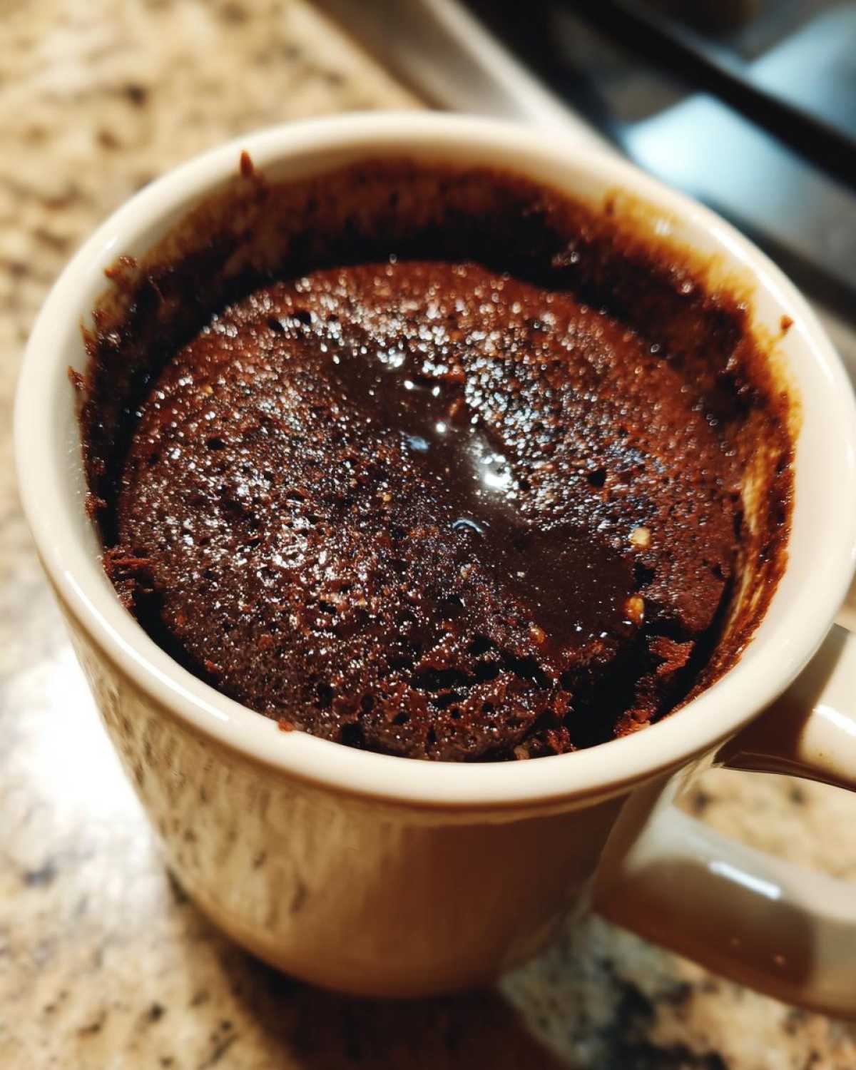 Close-up of a rich, fudgy chocolate mug cake baked inside a light-colored ceramic mug.