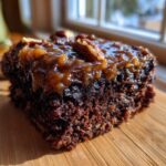 Close-up of a rich, moist slice of german chocolate poke cake topped with gooey caramel frosting and pecans.