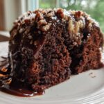 Close-up of a rich slice of german chocolate poke cake covered in gooey chocolate glaze and pecan coconut topping.
