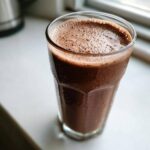 A tall, cold glass of homemade chocolate milk with a frothy top, condensation on the outside.