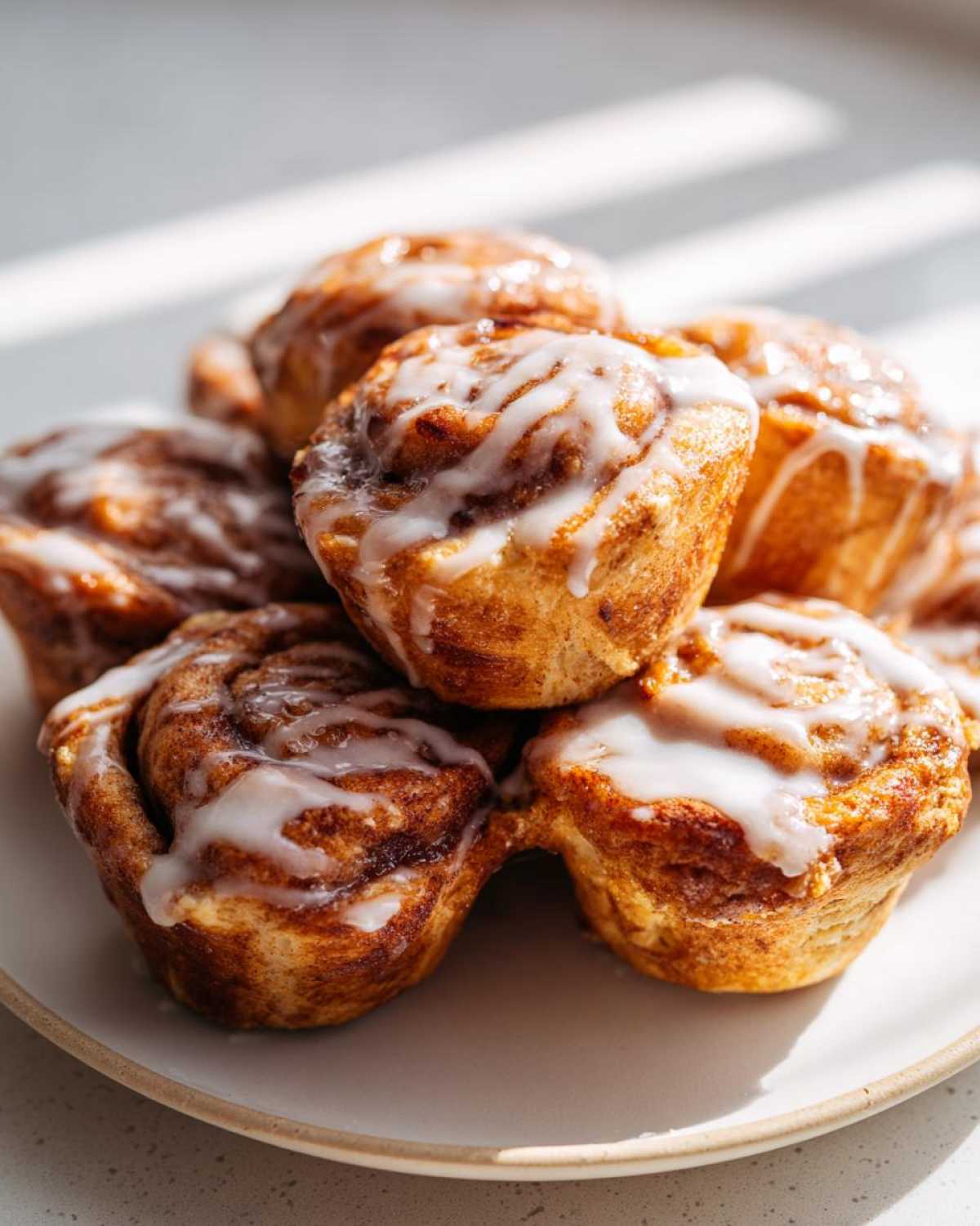 A close-up stack of freshly baked, gooey cinnamon roll bites drizzled with white icing.