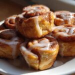 A stack of freshly baked, gooey cinnamon roll bites drizzled generously with white vanilla icing.