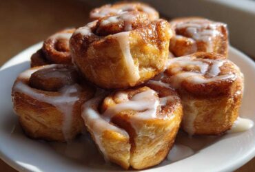 A stack of freshly baked, gooey cinnamon roll bites drizzled generously with white vanilla icing.