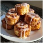 A stack of freshly baked, gooey cinnamon roll bites drizzled generously with white icing on a white plate.