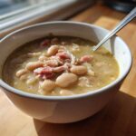 Close-up of a white bowl filled with rich ham and white bean soup, ready to eat.
