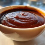 Close-up of thick, rich homemade brown gravy with swirling textures in a small white bowl.