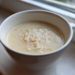 A close-up of creamy homemade cream of chicken soup topped with shredded chicken or noodles in a white mug.