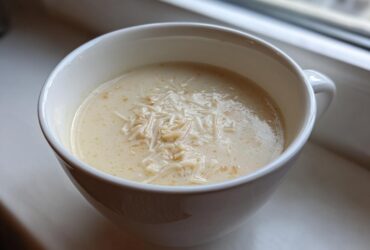 A close-up of creamy homemade cream of chicken soup topped with shredded chicken or noodles in a white mug.