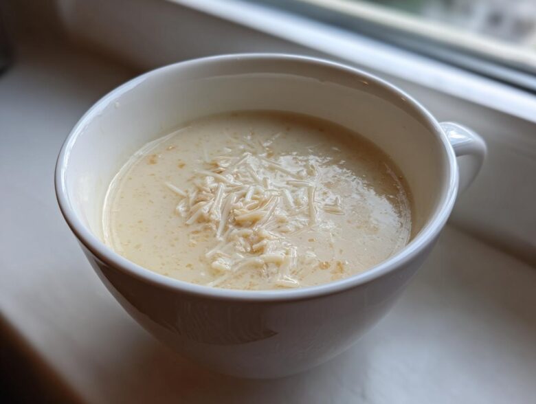 A close-up of creamy homemade cream of chicken soup topped with shredded chicken or noodles in a white mug.