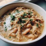 Close-up of a bowl of creamy instant pot white chicken chili topped with shredded chicken, white beans, sour cream, and fresh parsley.