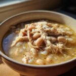 A close-up of a bowl filled with rich Instant Pot White Chicken Chili, featuring shredded chicken and white beans in a creamy broth.