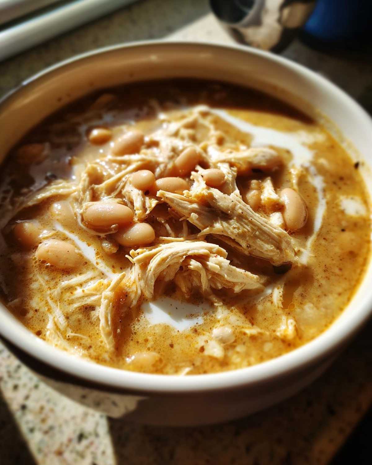 Close-up of a bowl of creamy instant pot white chicken chili topped with shredded chicken and white beans.