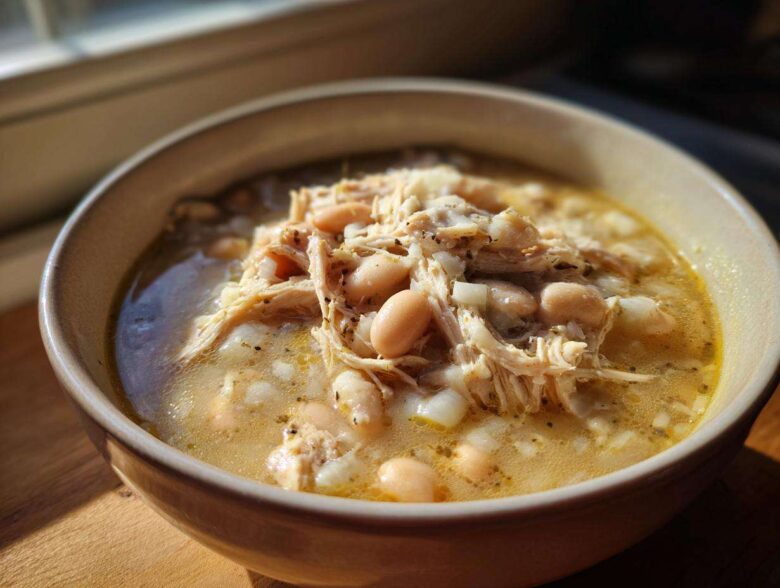 A close-up of a bowl filled with rich Instant Pot White Chicken Chili, featuring shredded chicken and white beans in a creamy broth.