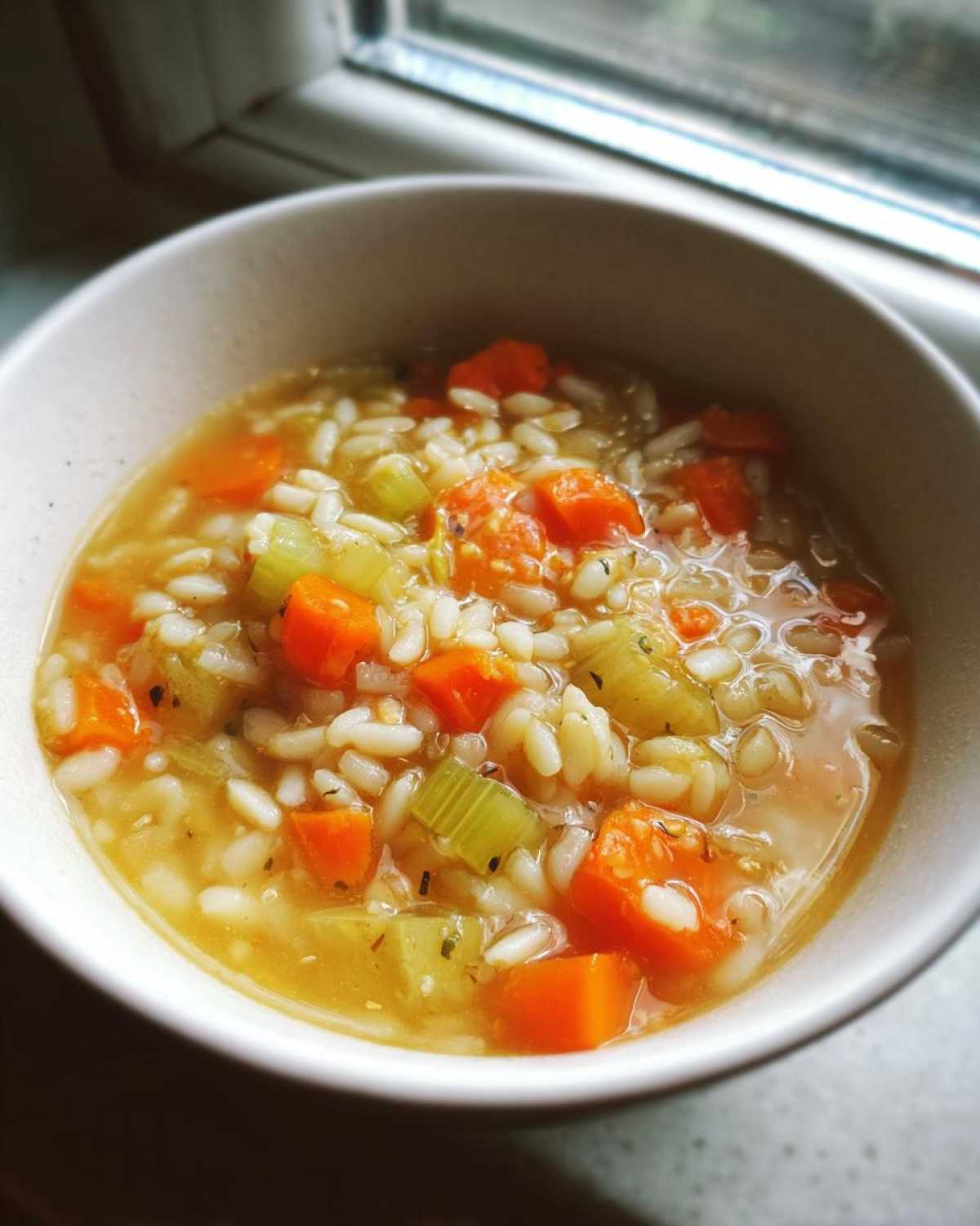 Close-up of a comforting bowl of italian penicillin soup filled with rice, diced carrots, and celery in broth.