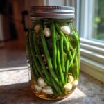 A glass jar packed tightly with fresh green beans, garlic cloves, and dill for making dilly beans.