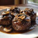 Four servings of juicy salisbury steak smothered in rich mushroom gravy on a white plate.
