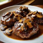Close-up of three rich, brown salisbury steak patties covered in thick mushroom gravy on a white plate.
