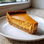 A perfect slice of keto pumpkin cheesecake with a thick crust, served on a white plate.