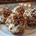 Four individual mini cheese ball recipe appetizers coated entirely in chopped pecans, served on a white plate.