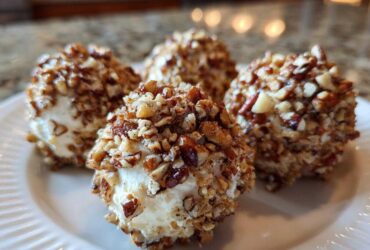 Four individual mini cheese ball recipe appetizers coated entirely in chopped pecans, served on a white plate.