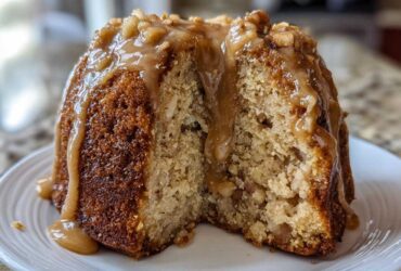 Close-up of a moist apple bundt cake slice drizzled with caramel glaze and topped with nuts.