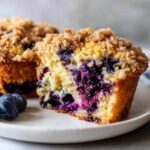 Close-up of a moist blueberry muffin cut in half, showing rich purple berries and a crunchy streusel topping.
