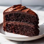 A close-up of a rich, moist slice of chocolate cake recipe covered in dark chocolate frosting.