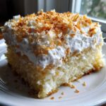 A moist slice of coconut poke cake topped with whipped cream and toasted coconut flakes.