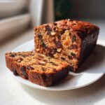 Close-up of a moist fruit cake recipe loaf, partially sliced, showing rich dried fruit and nuts.